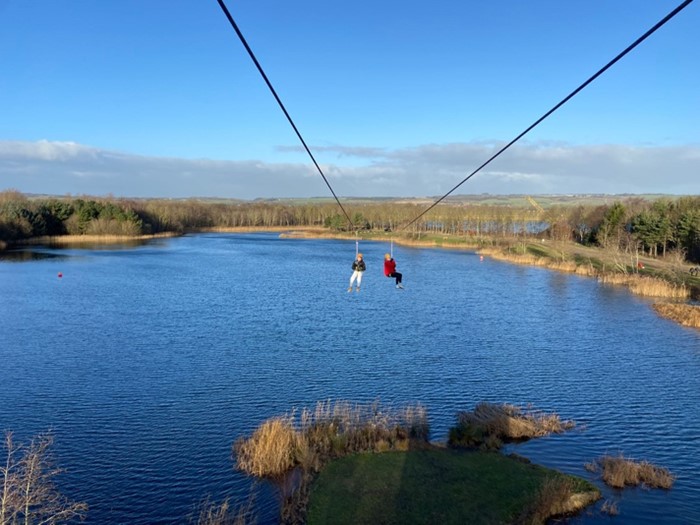 Two people on a zipline, over a lake.